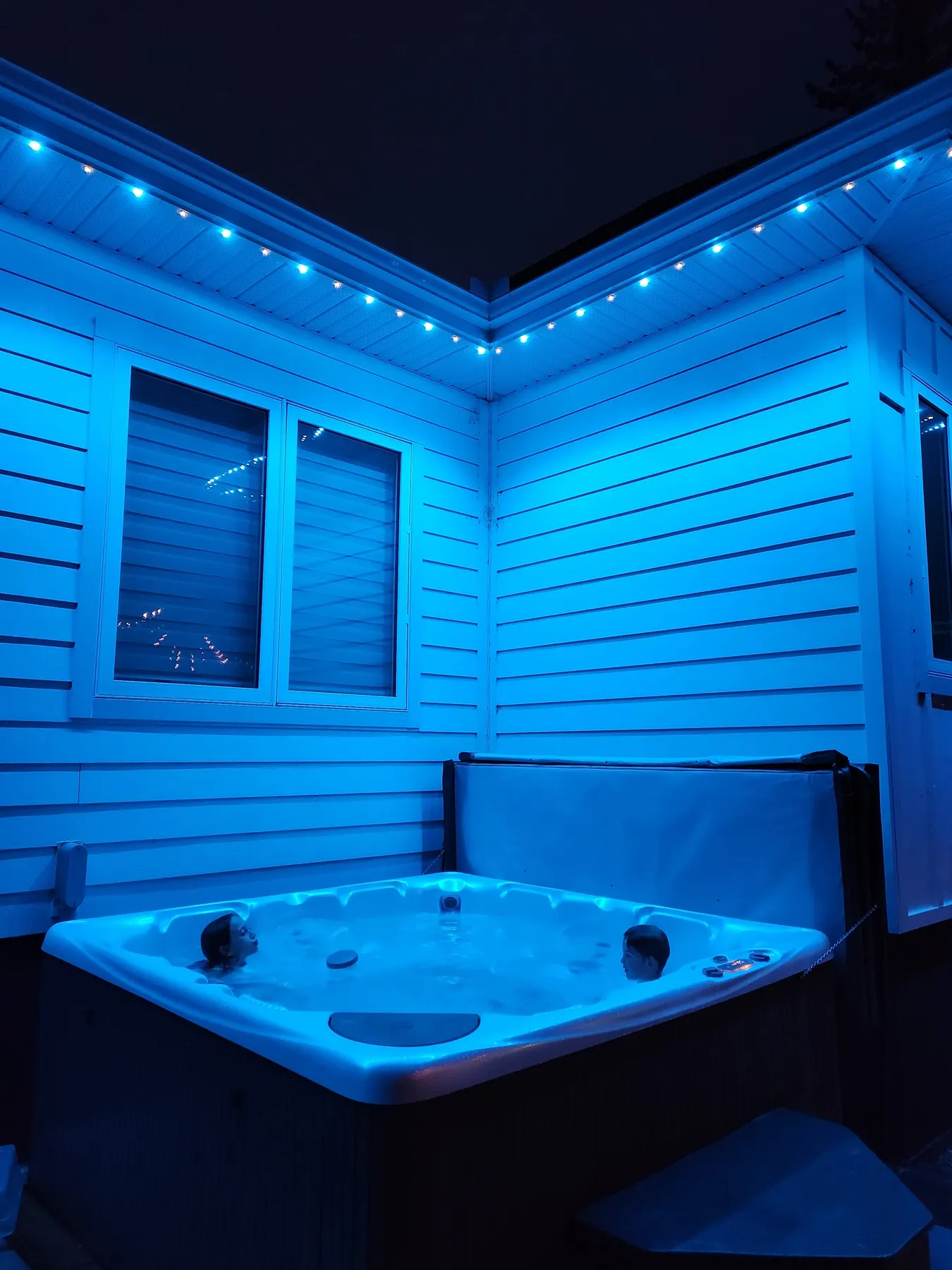 Teal permanent LED soffit lighting over a backyard hot tub